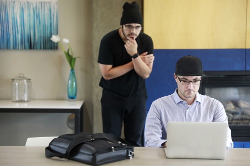 Man looking over another man's shoulder at his laptop.