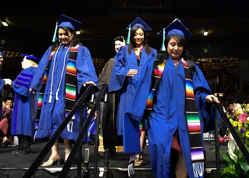 Three graduates in blue robes walking off stage