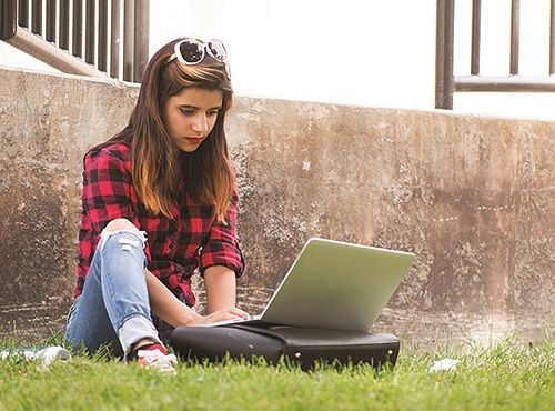 Student sitting in the grass while working on a laptop.