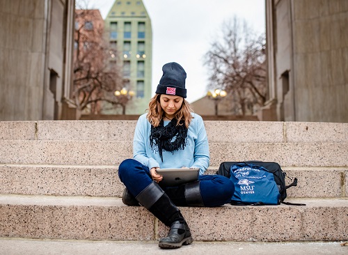 Student sitting on steps and working on laptop while wearing MSU Denver gear.