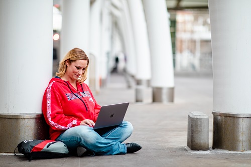 Student wearing Roadrunner gear studying on laptop outside Union Station.